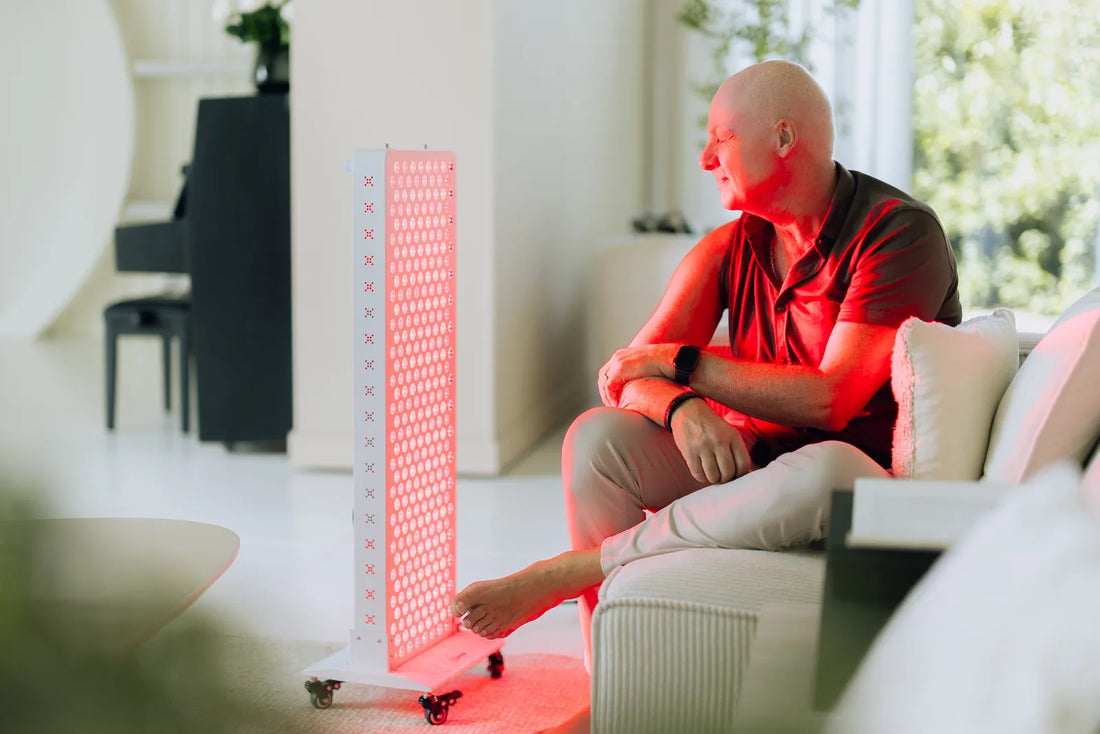 Man ontspant thuis op de bank naast een PrimeFORCE rood licht therapie paneel in een lichte woonkamer